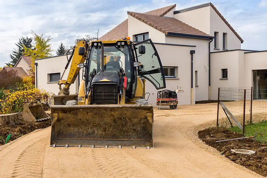 Bulldozer de polo-maçonnerie nivelant une allée en gravier devant maison moderne à Auch